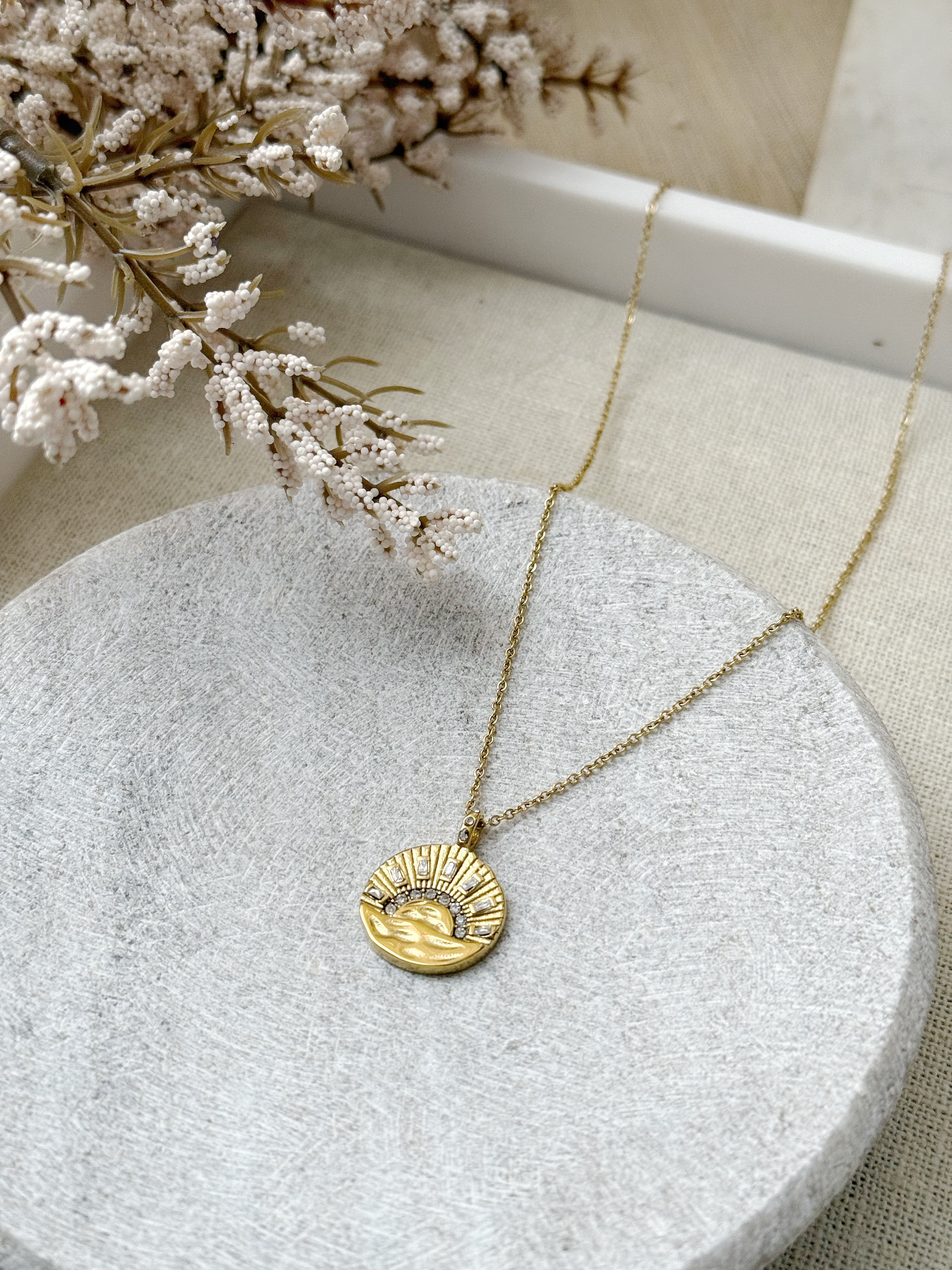 Gold necklace with a circular sunburst pendant